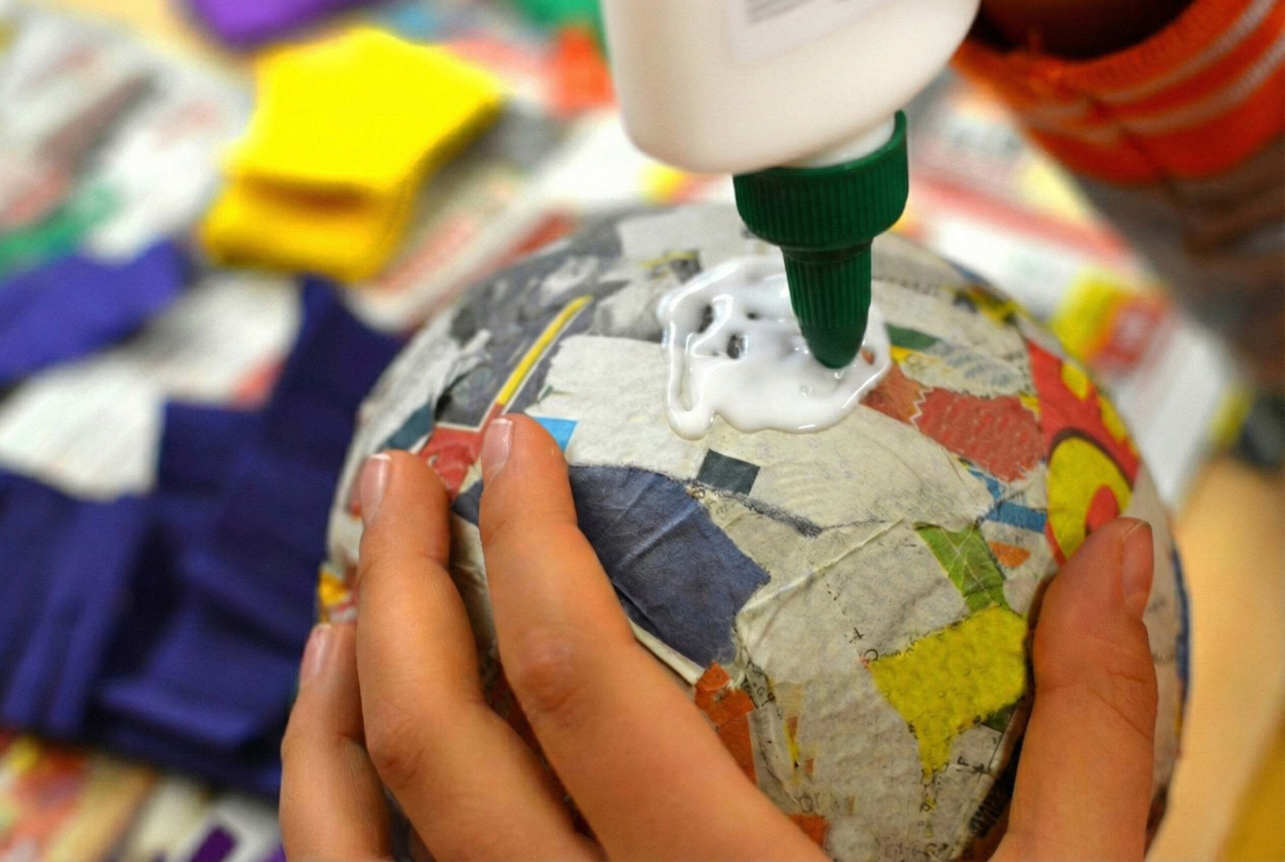 Close-up of hands applying school adhesive to a paper mâché craft, demonstrating bonding performance for classroom art projects.