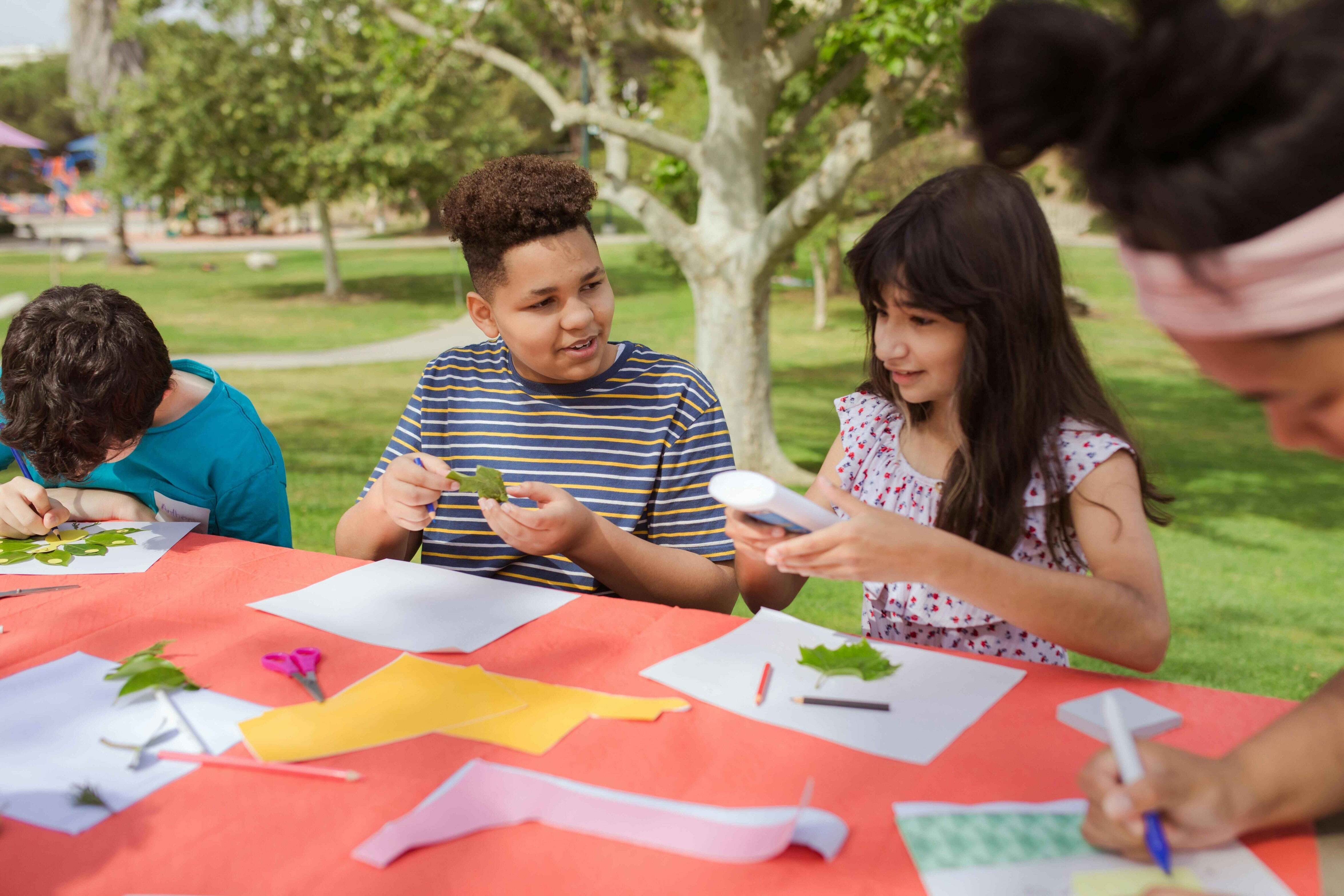 Children working together on an outdoor craft project using school adhesives, paper, and natural materials during a hands-on learning activity.