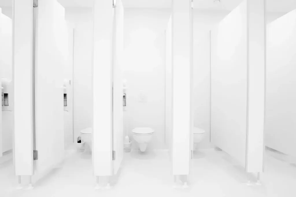 White public restroom toilet stalls with smooth walls and floors designed for durability and easier cleaning in high-traffic facilities.