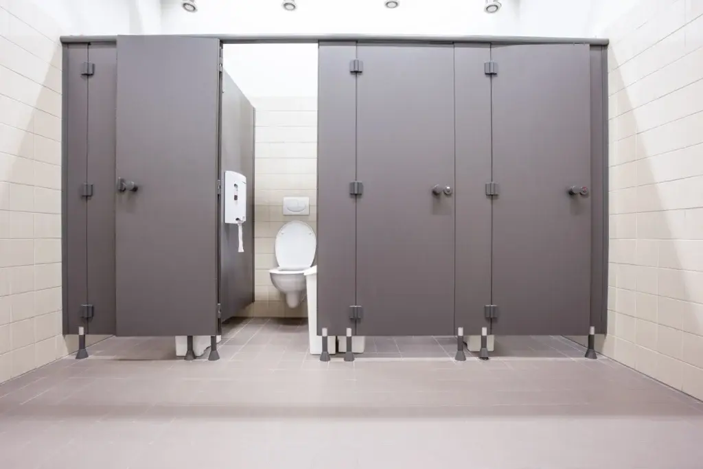Public restroom featuring gray toilet partitions and tiled floors built to withstand moisture, frequent cleaning, and heavy daily use.